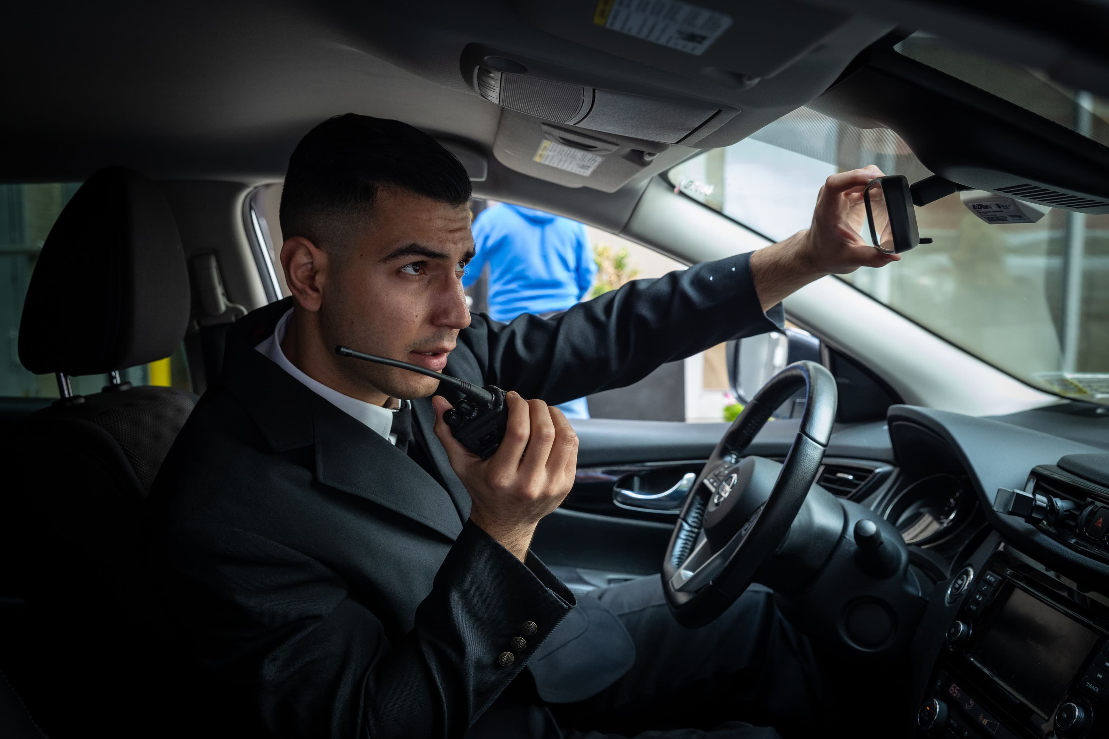 A security guard in a patrol vehicle, talking to a walkie talkie. 