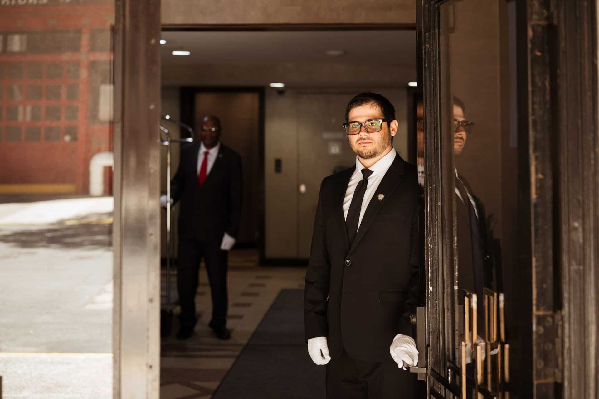 Uniformed white-glove staff greeting a resident at a building front entrance